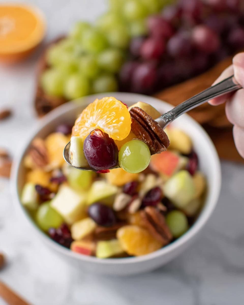 A close-up shows a spoon filled with vibrant fruit salad held by a woman's hand, hovering over a white bowl full of the same mix on a white marbled surface. The spoon contains a layered mix including a bright orange segment, light green apple cubes, dark red grapes, a brown pecan nut, and dark red dried cranberries. The fruit salad in the bowl below is a colorful mix of similarly textured and colored fruits, with green grapes and small fruit pieces visible. In the background, there is a blurred cluster of green and red grapes, adding depth to the image. Photo taken with an iphone --ar 4:5 --v 7