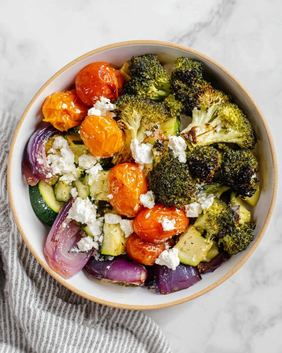 A white bowl filled with a colorful roasted vegetable mix sits on a white marbled surface. The base layer shows chopped soft green zucchini and chunks of roasted purple onion scattered around. On top, there are bright orange roasted cherry tomatoes, slightly wrinkled with softness. Green broccoli florets with some charred tips are placed over the veggies, adding texture and height. Crumbled white cheese is spread through the bowl, contrasting with the deep greens and warm colors. The bowl is simple with a thin beige rim, and a gray striped cloth is partially visible to one side. photo taken with an iphone --ar 4:5 --v 7