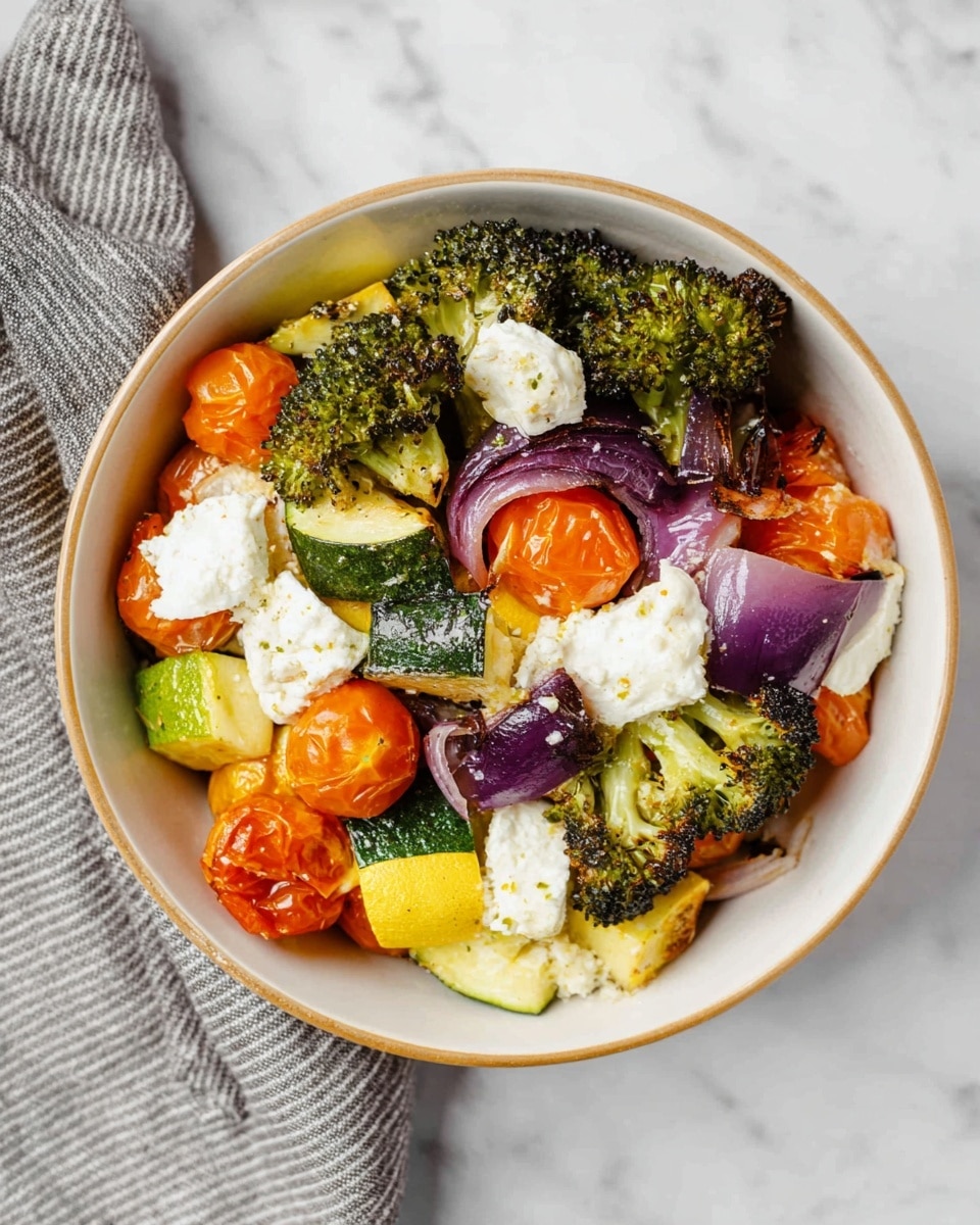 A bowl filled with layers of roasted vegetables and cheese sits on a white marbled surface. The bottom layer is made of chopped green zucchini and yellow squash with a slightly roasted look. Above that are orange cherry tomatoes that are roasted with wrinkled skins, scattered around the bowl. There are pieces of purple-red onion and some charred green broccoli florets layered on top. White pieces of soft cheese are placed among the vegetables, adding a creamy texture. The bowl is white with a light brown rim, and a gray striped cloth is partially visible to the left. Photo taken with an iphone --ar 4:5 --v 7