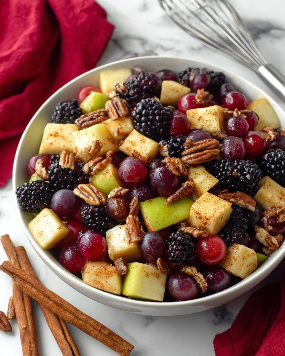 A close-up of a fruit salad in a white bowl filled with layers of different fruits and nuts. The bottom layer has dark purple-black blackberries, followed by shiny red grapes scattered throughout. On top, there are light yellow apple chunks sprinkled with a brown spice that looks like cinnamon, mixed with small pieces of pecans. The bowl is placed on a white marbled surface with two cinnamon sticks lying next to it, and a metal whisk and red cloth visible in the background. photo taken with an iphone --ar 4:5 --v 7