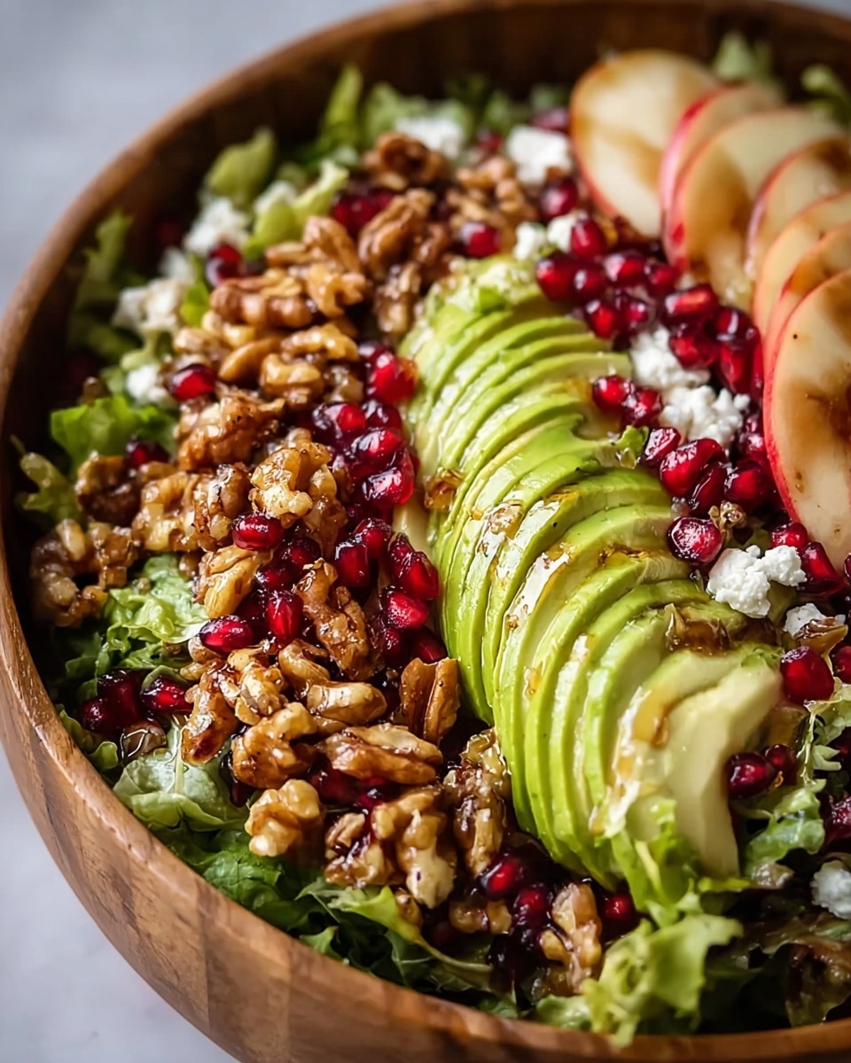 A wooden bowl filled with a fresh salad, layered with curly green lettuce as the base. On top, there are thin slices of light green avocado arranged in a fan shape, scattered deep red pomegranate seeds adding bright pops of color, and crumbled white cheese dotted throughout. Toasted golden-brown walnuts are spread all over, giving a crunchy texture. A few slices of peeled apple with red edges are tucked on the side inside the bowl. The whole salad has a light shiny glaze, suggesting a drizzle of dressing. photo taken with an iphone --ar 4:5 --v 7