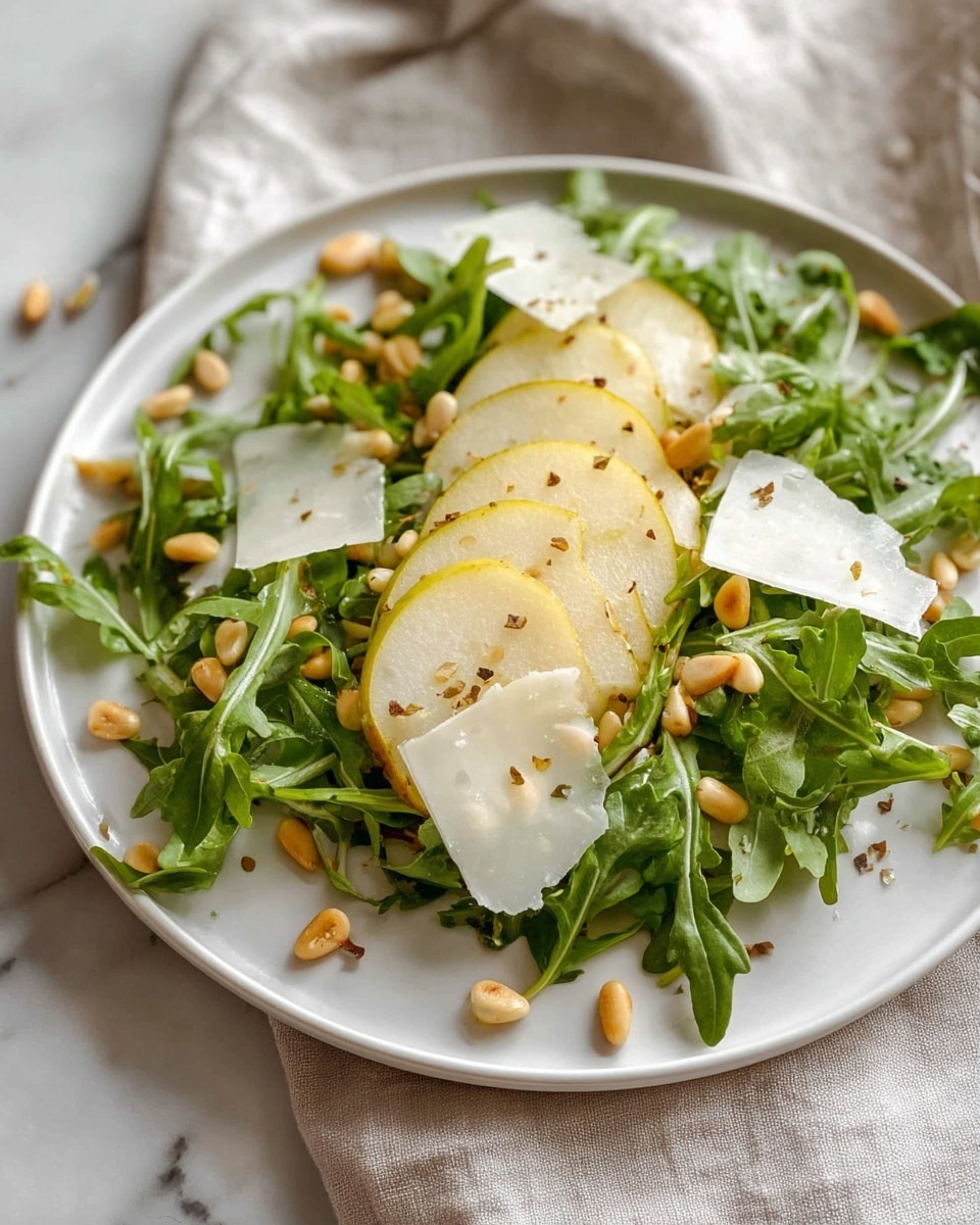 A fresh salad is shown on a white plate, layered with bright green arugula leaves spread evenly as the base. On top, there are thin slices of light yellow pear with a slightly rough skin, positioned in a scattered way. Small golden pine nuts are sprinkled around, adding texture and color contrast. Thin, irregular white cheese shavings are placed across the salad. The salad looks lightly seasoned with cracked black pepper and some small grains of salt. The plate is set on a soft, light-colored cloth over a white marbled surface. photo taken with an iphone --ar 4:5 --v 7