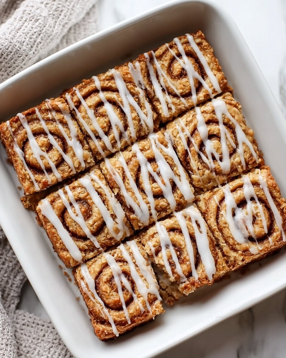 Six rectangular pieces of baked cinnamon swirl oatmeal bars are inside a white square dish. Each bar shows a clear spiral pattern of cinnamon in the middle, with a golden-brown oat texture around it. A white glaze is drizzled evenly across the top of all bars in thin stripes. The dish sits on a white marbled surface with a soft textured cloth partially visible in the corner. photo taken with an iphone --ar 4:5 --v 7