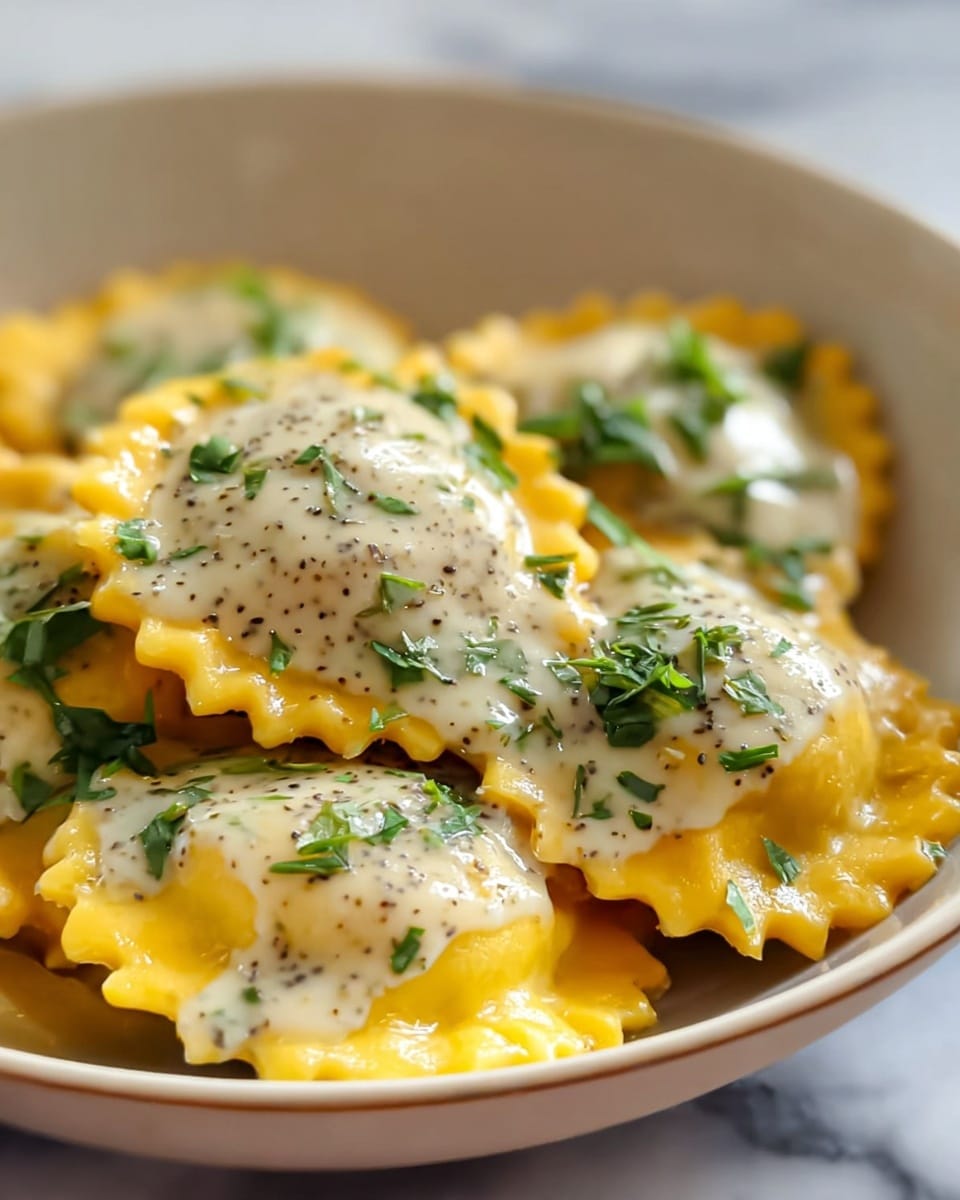 A close-up image showing six round ravioli pieces in a white bowl, each with bright yellow pasta that has ruffled edges. On top of each ravioli is a light cream sauce speckled with black herbs or spices, giving a textured, creamy look. Fresh green herbs are sprinkled over the sauce and ravioli, adding a pop of color. The bowl sits on a white marbled surface that is softly blurred in the background. photo taken with an iphone --ar 4:5 --v 7