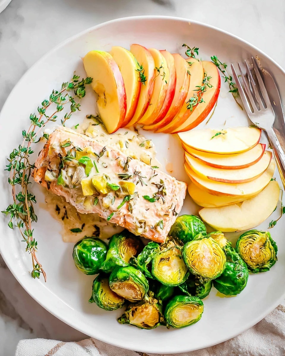 On a white plate with a silver fork resting on the edge, a piece of cooked pork is topped with a creamy white sauce speckled with herbs and small browned bits, sitting on a sprig of fresh green rosemary and thyme. To the right of the pork are 3 thin slices of pale yellow apple with smooth shiny skin. On the bottom right of the plate, there is a pile of bright green Brussels sprouts, some sliced in half showing tender inner layers and some whole with a slight char. On the left side, more slices of apple are visible next to the pork with more fresh herb sprigs scattered around. The surface beneath is a white marbled texture. In the background, out of focus, is a wooden bowl with green vegetables and a white dish with sauce. Photo taken with an iphone --ar 4:5 --v 7
