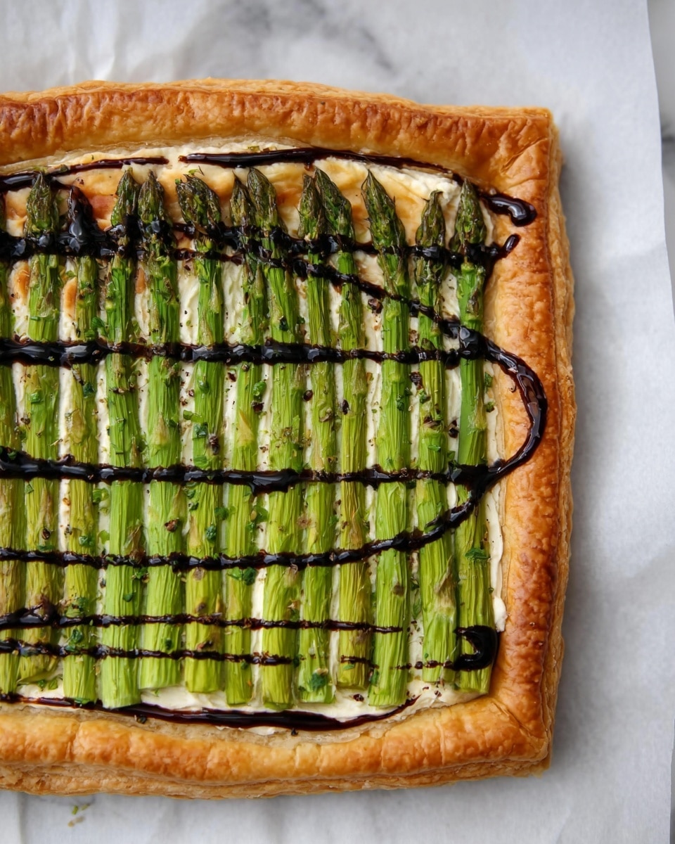 A rectangular puff pastry tart with a golden-brown, crispy crust forms the base layer, around an inch thick at the edges. Inside, a layer of creamy white cheese covers the pastry evenly. On top of the cheese, bright green asparagus spears are laid parallel in neat rows covering the entire middle section of the tart. A dark, glossy balsamic glaze is drizzled in curved lines across the asparagus, adding contrast and shine. The tart is placed on a white marbled surface with the right edge slightly cropped out of the frame. Photo taken with an iphone --ar 4:5 --v 7