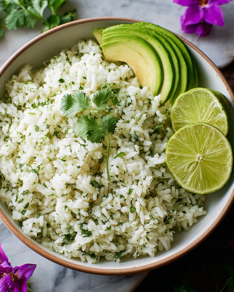 A close-up of a bowl filled with fluffy white rice mixed with small green cilantro leaves and tiny bits of lime zest scattered throughout, giving a fresh and light appearance. On the left side inside the bowl, several slices of green avocado and two lime wedges rest against the rice. The bowl is white with a light brown rim, placed on a surface with a white marbled texture. A few sprigs of cilantro and a bright purple flower are near the bowl, adding natural color contrast. photo taken with an iphone --ar 4:5 --v 7