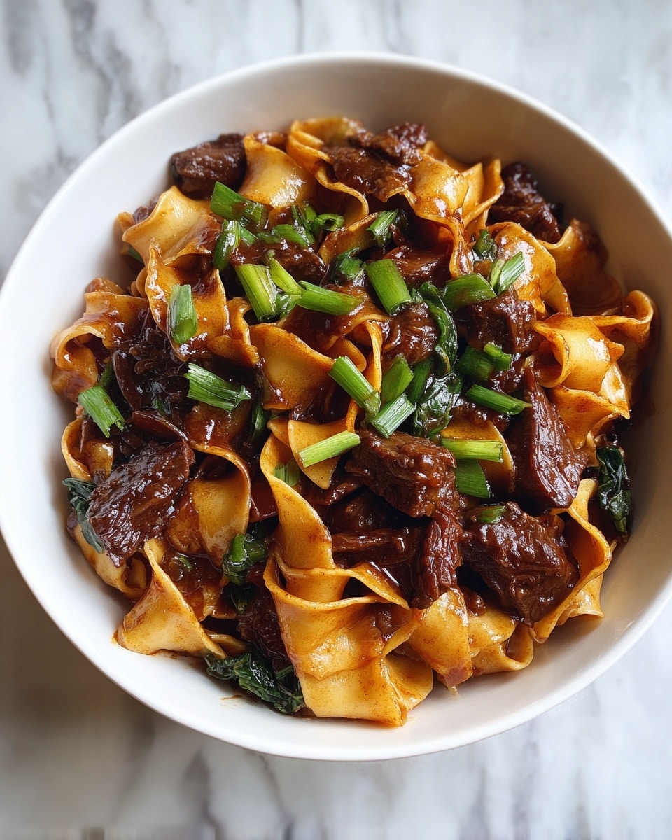 This image shows a white bowl filled with thick, flat noodles mixed with dark brown chunks of beef coated in a shiny sauce. Bright green chopped herbs are scattered on top, adding a fresh pop of color. The noodles have a slightly glossy texture and are twisted around each other, while the beef pieces look tender and juicy. The bowl is placed on a white marbled surface, making the rich colors of the food stand out clearly. photo taken with an iphone --ar 4:5 --v 7
