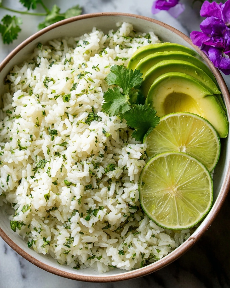 A bowl of white rice mixed with finely chopped green herbs like cilantro, giving a speckled green and white appearance, topped with a few fresh cilantro leaves for garnish; on one side inside the bowl, there are slices of green avocado fanned out next to two lime wedges; the bowl is white with a light brown rim, and the whole setup is placed on a white marbled surface with a purple flower near the bottom right corner; photo taken with an iphone --ar 4:5 --v 7