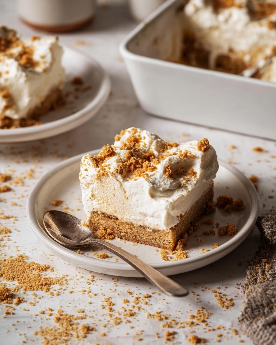 The image shows a slice of dessert on a white plate with a crumbly light brown base layer soaked in syrup, topped with a thick, fluffy white whipped cream layer, and sprinkled with crushed golden-brown cookie crumbs on top and around the plate. The dessert slice is soft and moist, with a spoon next to it on the plate. In the background, there is another similar white plate with a slice of the same dessert and a white rectangular baking dish filled with the dessert, both resting on a white marbled textured surface. Photo taken with an iphone --ar 4:5 --v 7