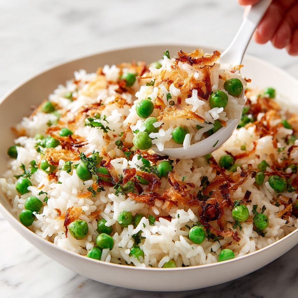 A white bowl filled with fluffy white rice mixed with small green peas and bits of light golden fried onions scattered throughout, creating a mix of white, green, and light golden colors. A woman's hand holds a spoon scooping up a portion of the rice, showing the soft texture of the grains and the evenly distributed vegetables. The bowl rests on a white marbled surface. The photo taken with an iphone --ar 4:5 --v 7