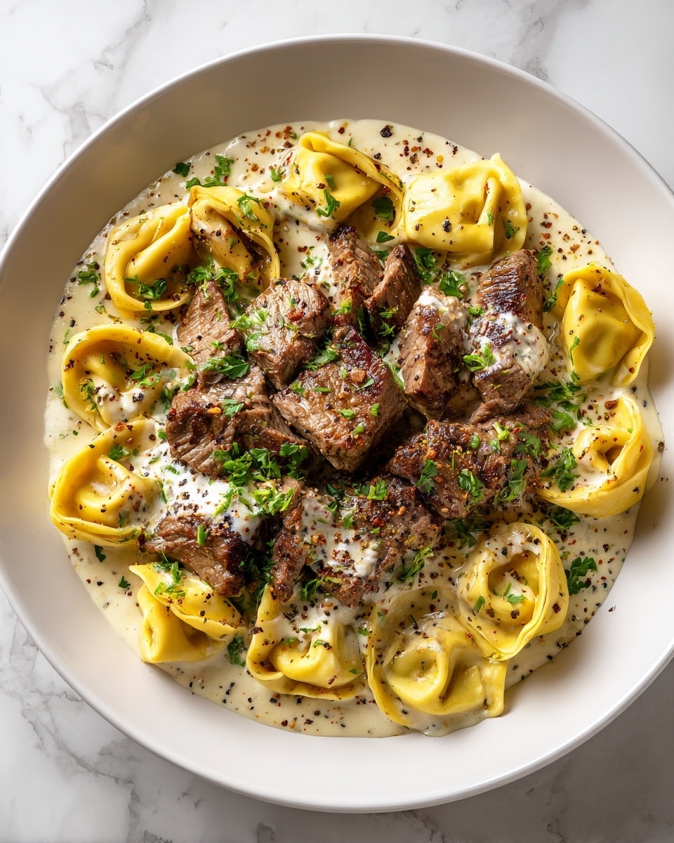 The dish shows a close-up of a white plate filled with creamy sauce at the bottom, light beige with specks of black pepper, creating a smooth texture. On top of the sauce, there are yellow tortellini pasta arranged around dark brown, seared beef chunks with visible grill marks. The beef pieces are placed mainly in the center, slightly overlapping the pasta. Small green herb bits are sprinkled lightly over the sauce, pasta, and beef, adding a fresh touch. The sauce glistens in places where it covers the meat and pasta. photo taken with an iphone --ar 4:5 --v 7