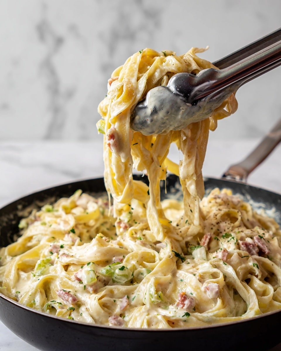 The image shows a close-up of creamy, pale yellow pasta with small pieces of light pink ham mixed evenly throughout, all being lifted from a black pan with black-tipped tongs. The pasta strands are flat and slightly curly in texture, coated in a thick, smooth sauce that has a glossy shine. The pan beneath contains a generous layer of the same creamy pasta and ham mixture, with visible soft, pale green bits that might be vegetable pieces. The background has a white marbled texture that adds brightness to the scene. photo taken with an iphone --ar 4:5 --v 7