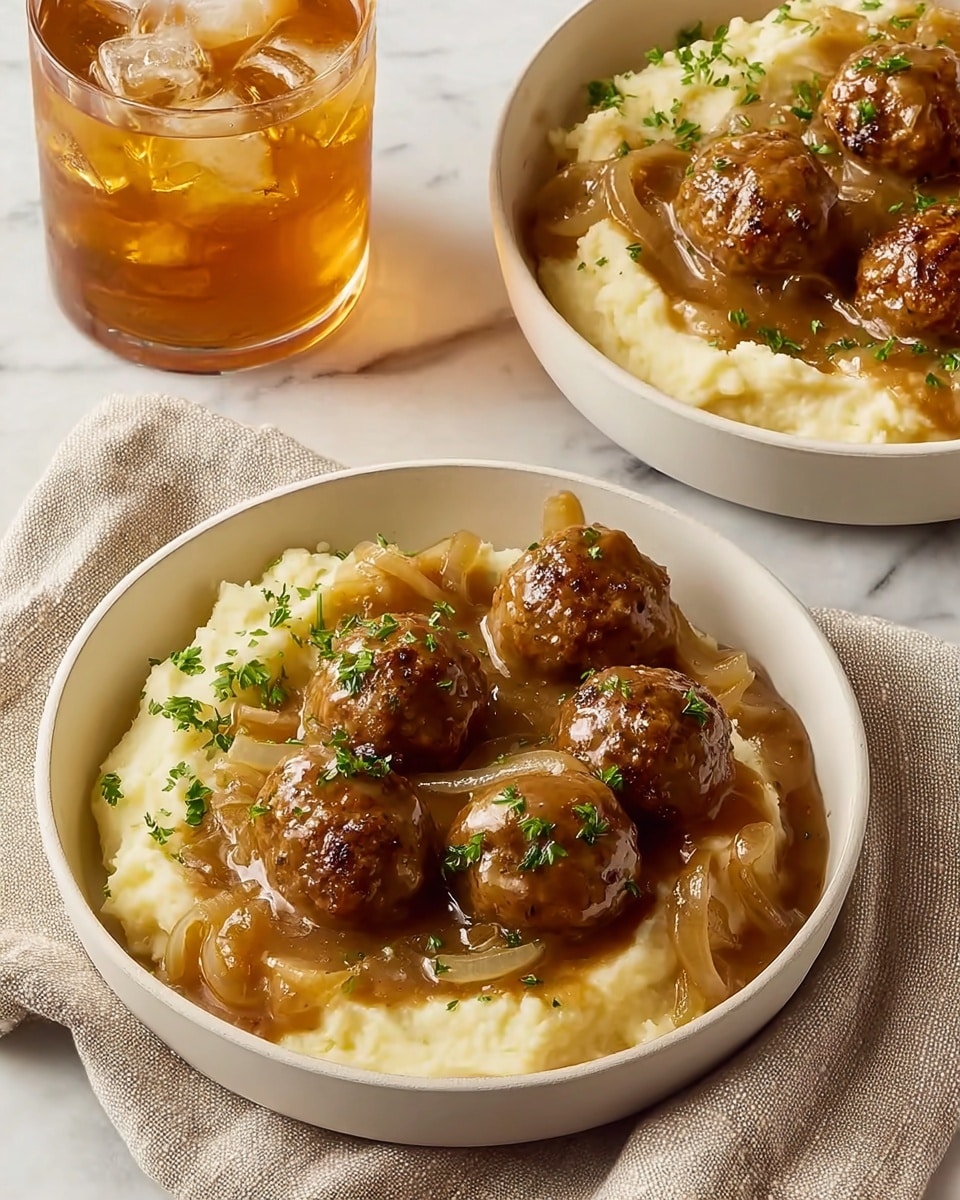 Two bowls filled with a meal are placed on a beige cloth over a white marbled surface. Each white bowl has a base layer of creamy mashed potatoes, pale yellow with a smooth texture, arranged on one side. On top and beside the mashed potatoes, there are six round meatballs coated in a thick brown gravy with visible slices of cooked onions. The gravy is glossy and covers part of the mashed potatoes, with finely chopped green herbs sprinkled over the dish. In the upper left, a glass filled with iced tea and ice cubes adds a refreshing contrast. Photo taken with an iphone --ar 4:5 --v 7