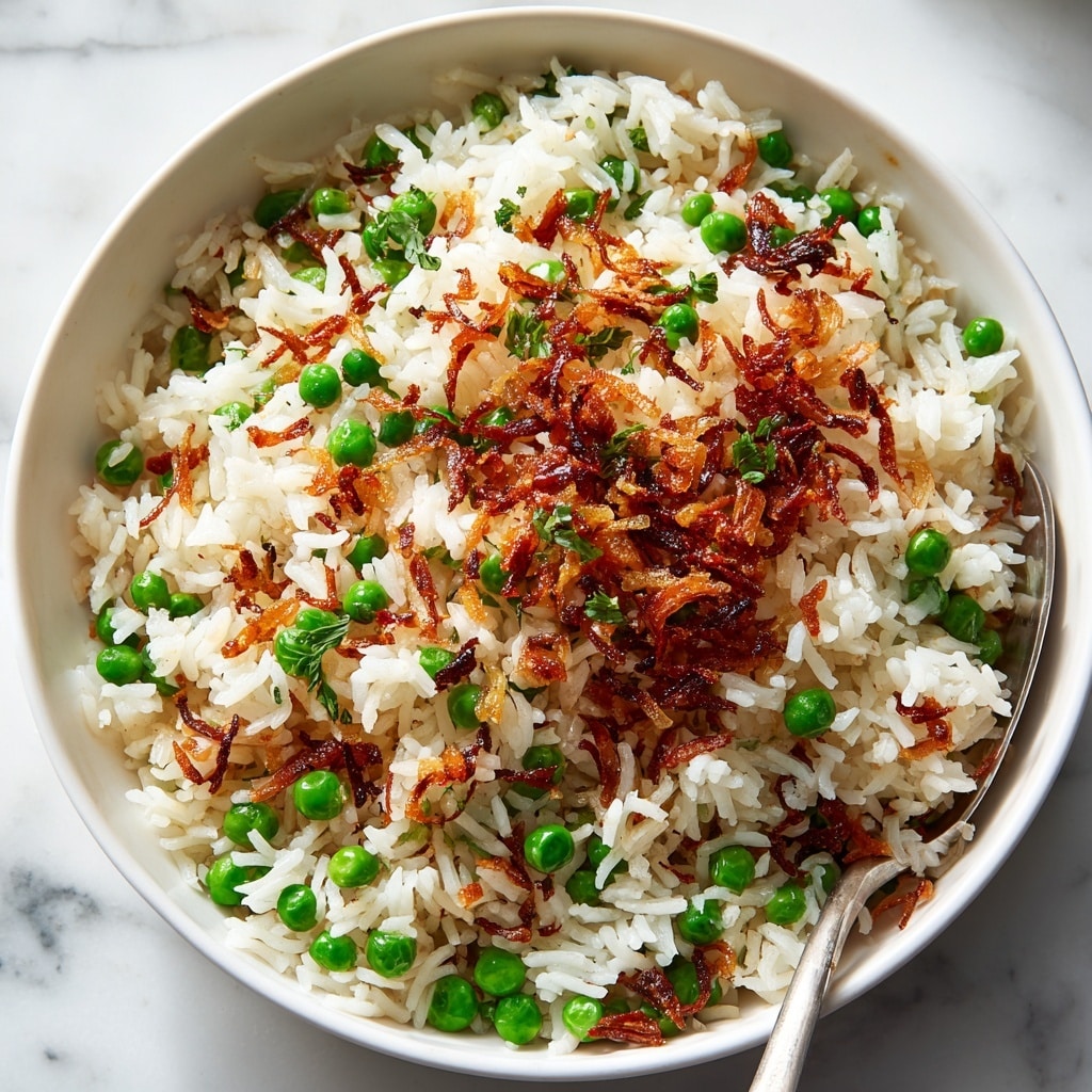 A close-up of a white bowl filled with cooked white rice mixed with green peas and small bits of browned onions, topped with crispy fried onions that add a golden color and crunchy texture. A white spoon is scooping a portion of the rice from the bowl, showing the fluffy texture of the rice and vibrant green peas underneath. The bowl sits on a white marbled surface. photo taken with an iphone --ar 4:5 --v 7