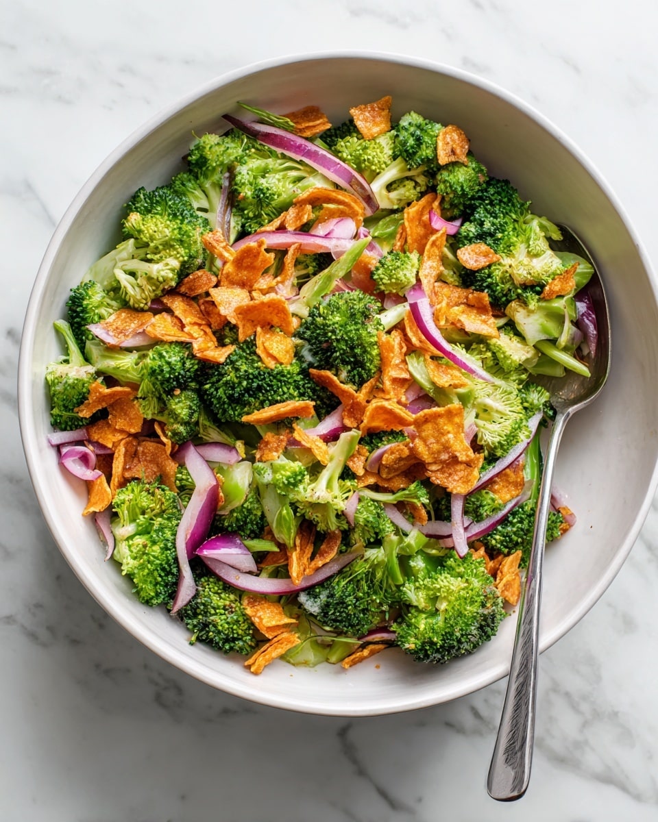 A white plate filled with a colorful broccoli salad showing three main layers: bright green broccoli florets as the base layer, scattered small pieces of chopped purple onions and thin, sliced orange carrots on top, and lightly sprinkled crispy, golden brown bacon bits covering the salad. A silver spoon rests on the right side of the plate. The plate sits on a white marbled surface. photo taken with an iphone --ar 4:5 --v 7