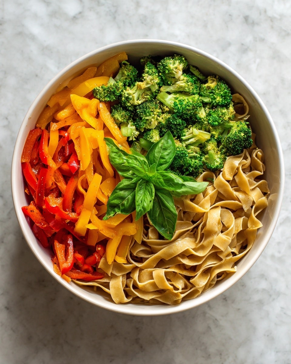 The image shows a white bowl filled with three layers of colorful food. The bottom layer has flat, light brown noodles that look soft and wide. On top of the noodles, there are bright orange and yellow strips of bell peppers mixed with green broccoli pieces that add a fresh texture and color contrast. The top layer has a small bunch of fresh green basil leaves in the center that adds a fresh touch. The background is a white marbled surface. photo taken with an iphone --ar 4:5 --v 7