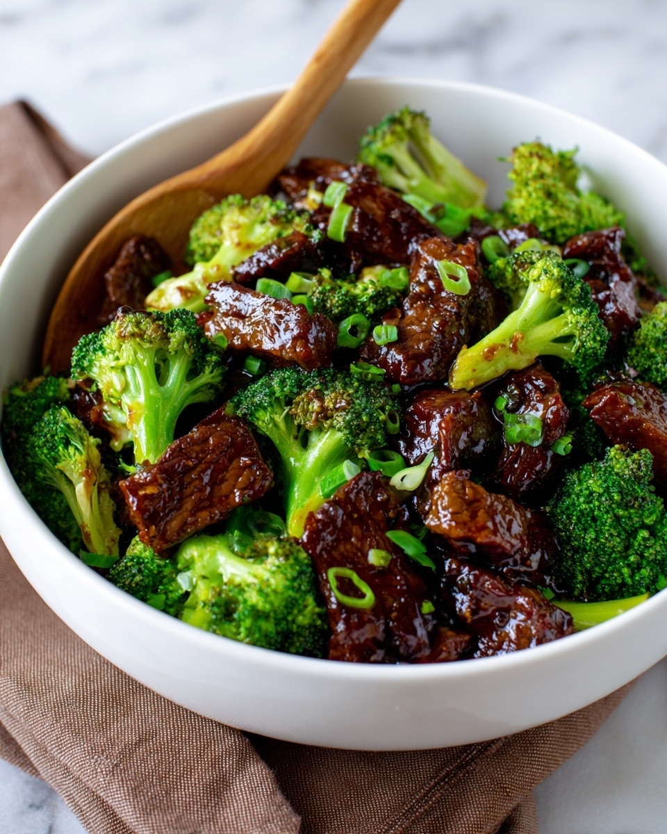 A white bowl holds a stir fry dish with two main layers: shiny, dark brown pieces of beef mixed with fresh, bright green broccoli florets. The beef is cut into medium-sized, uneven rectangular strips with a glossy sauce coating, while the broccoli looks crisp and vibrant, creating a fresh contrast. Tiny bits of chopped green onions add a slight touch of light green scattered on top. A wooden spoon rests partly in the bowl on the left side. The bowl sits on a white marbled textured surface with a folded brown cloth beneath it. Photo taken with an iphone --ar 4:5 --v 7
