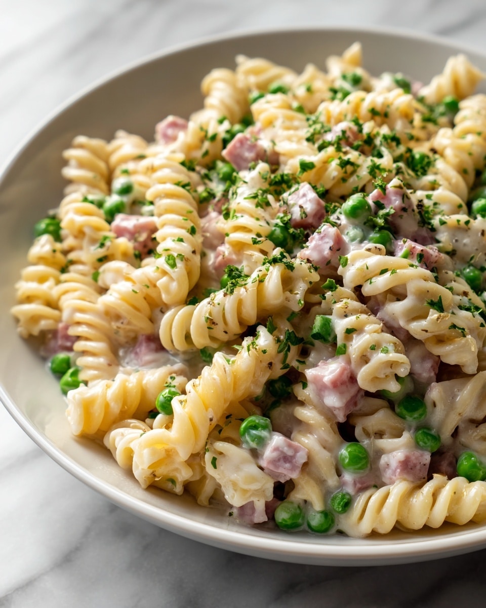 The image shows a bowl filled with creamy pasta made of short spiral noodles mixed with small pieces of cooked ham and finely chopped green herbs on top. The pasta has a smooth, creamy light yellow sauce that coats each noodle, and the ham adds a pinkish color contrast. The bowl is white, and it sits on a white marbled surface. Photo taken with an iphone --ar 4:5 --v 7