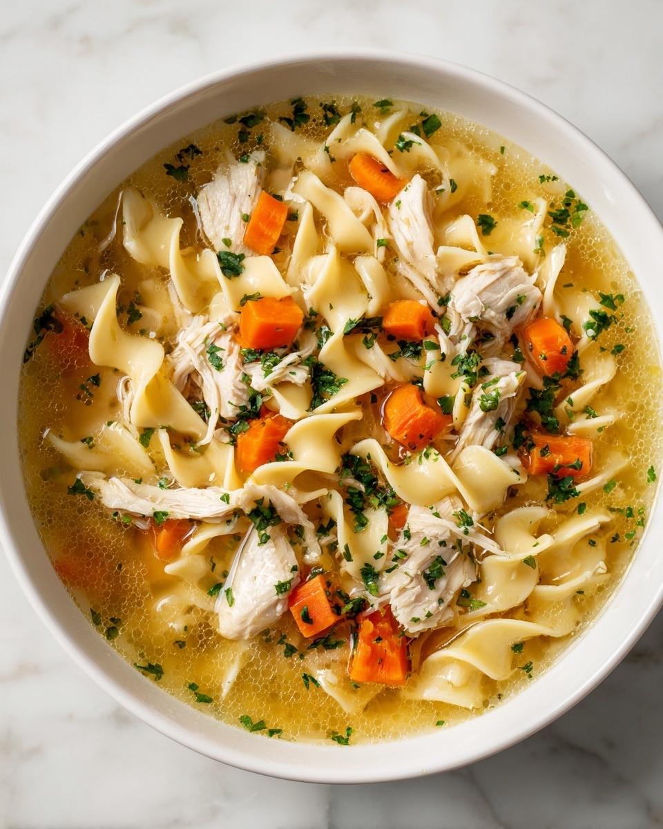 A white bowl filled with chicken noodle soup is shown, containing three visible layers: the base layer is a clear yellow broth with small bubbles, the middle layer consists of thick yellow egg noodles curling throughout the soup, and the top layer shows shredded white chicken pieces and small diced orange carrots scattered evenly, all garnished with fresh green parsley finely chopped and sprinkled on top. The bowl rests on a white marbled surface that is softly lit, creating a warm and inviting scene. Photo taken with an iphone --ar 4:5 --v 7