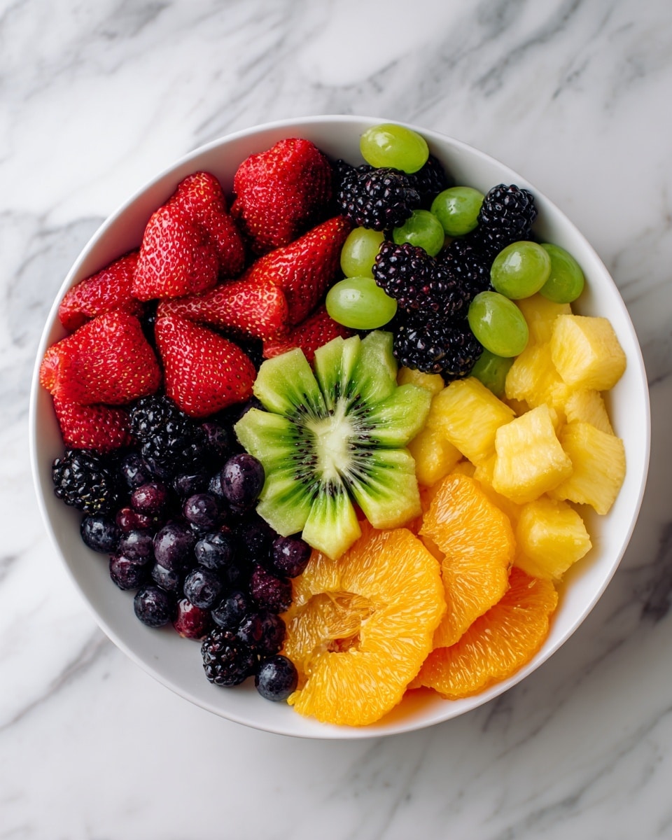 A white plate filled with a colorful fruit arrangement on a white marbled surface. The bottom layer consists of green grapes and red grapes spread evenly. On top are slices of bright orange, yellow pineapple shaped like flowers, kiwi with green flesh and black seeds, and large red strawberries, some halved. Clusters of dark blueberries and blackberries fill spaces between the larger fruits. In the foreground, cherries are cut in half and arranged to look like a red flower. The fruits have a fresh, juicy texture. Photo taken with an iphone --ar 4:5 --v 7
