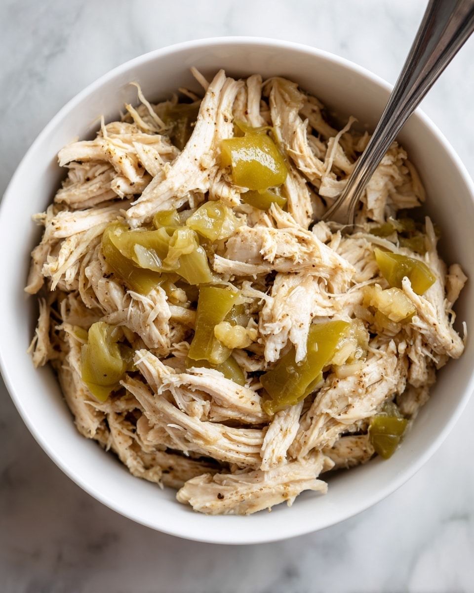 The image shows a white bowl filled with shredded cooked chicken mixed with soft, cooked green peppers. The chicken looks tender and moist, with a light brown color from the cooking juices, while the green peppers add a shiny, slightly wrinkled texture on top and throughout the chicken. A fork is resting inside the bowl at the top right side, and a woman's hand is holding the bowl from the left side. The background is a white marbled texture. Photo taken with an iphone --ar 4:5 --v 7