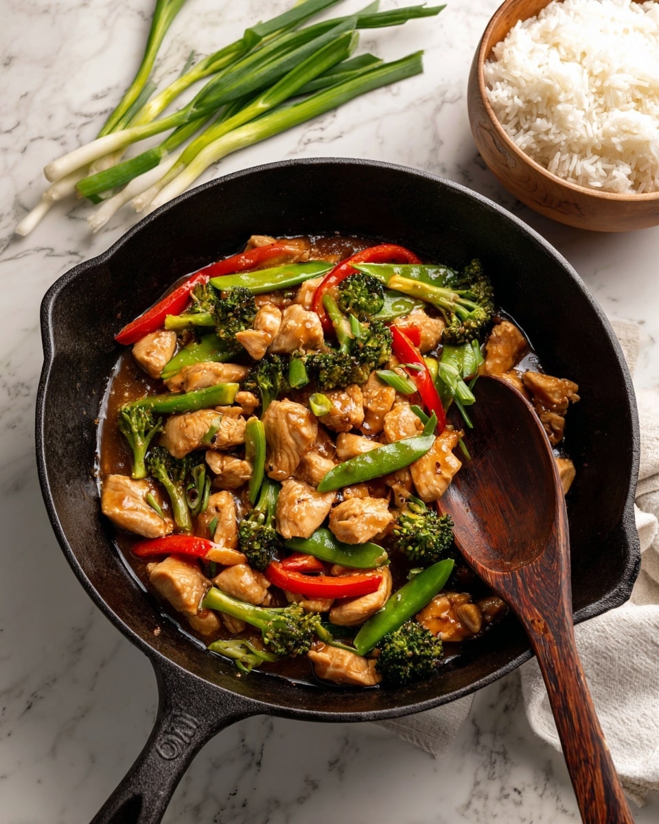 A black cast iron pan filled with a stir-fry showing multiple layers of glossy, cooked ingredients, including chunks of light brown chicken, bright green broccoli florets, crisp green snow peas, and long strips of red bell pepper scattered evenly throughout a medium brown, thick sauce. A wooden spoon with a dark handle lies inside the pan, partially covered by the food. To the top right, fresh green onions rest on a white marbled surface, while in the top left corner, a white bowl of cooked white rice with chopsticks is partially visible. The overall image gives a fresh, colorful, and savory look. Photo taken with an iphone --ar 4:5 --v 7