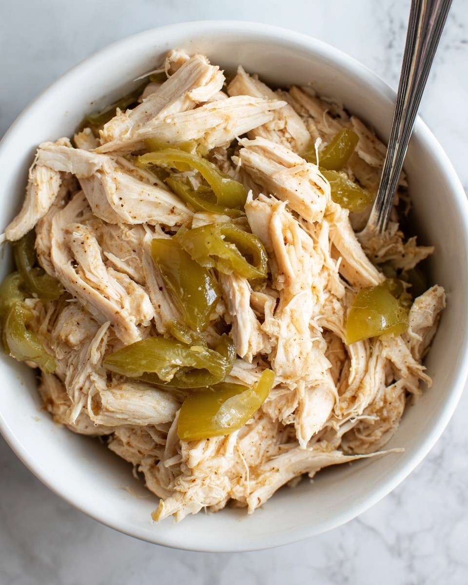 The image shows a close-up of a white bowl filled with shredded chicken pieces mixed with light green pepper slices on top. The chicken has a soft, moist texture with some brown seasoning visible, and the peppers appear glossy and tender. A metal fork rests inside the bowl, and the bowl sits on a white marbled surface. The overall colors are light brown, pale green, and white, with the food looking fresh and savory. Photo taken with an iphone --ar 4:5 --v 7