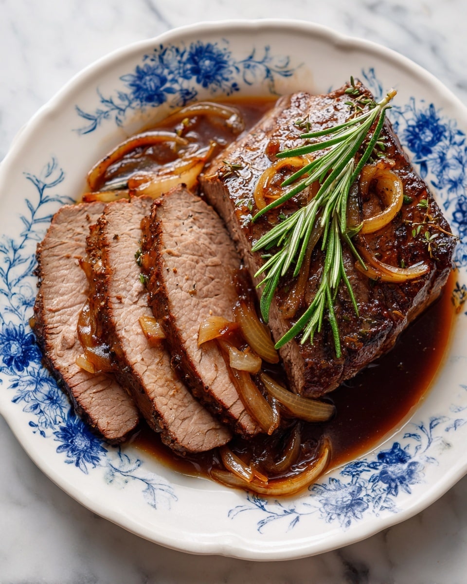 A large piece of cooked beef roast sits on a white plate with blue floral design, with the left side sliced into thick layers showing a tender, moist, and slightly pink interior with a brown crusty edge. On top of the beef are several caramelized, translucent onion slices with a shiny texture and a green sprig of fresh rosemary resting diagonally, adding a fresh contrast. The beef rests in a small pool of rich brown sauce, partially surrounding the meat and onions. The plate sits on a surface with white marbled texture. photo taken with an iphone --ar 4:5 --v 7