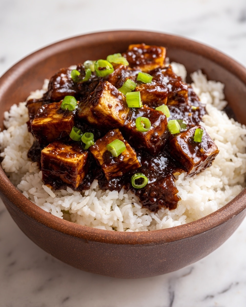 A brown bowl filled with one bottom layer of white cooked rice showing soft, slightly separated grains, topped with a thick second layer of small, glossy, golden-brown tofu cubes coated in a rich dark brown sauce, and finished with chopped bright green scallions scattered evenly on top; the bowl sits on a white marbled surface photo taken with an iphone --ar 4:5 --v 7