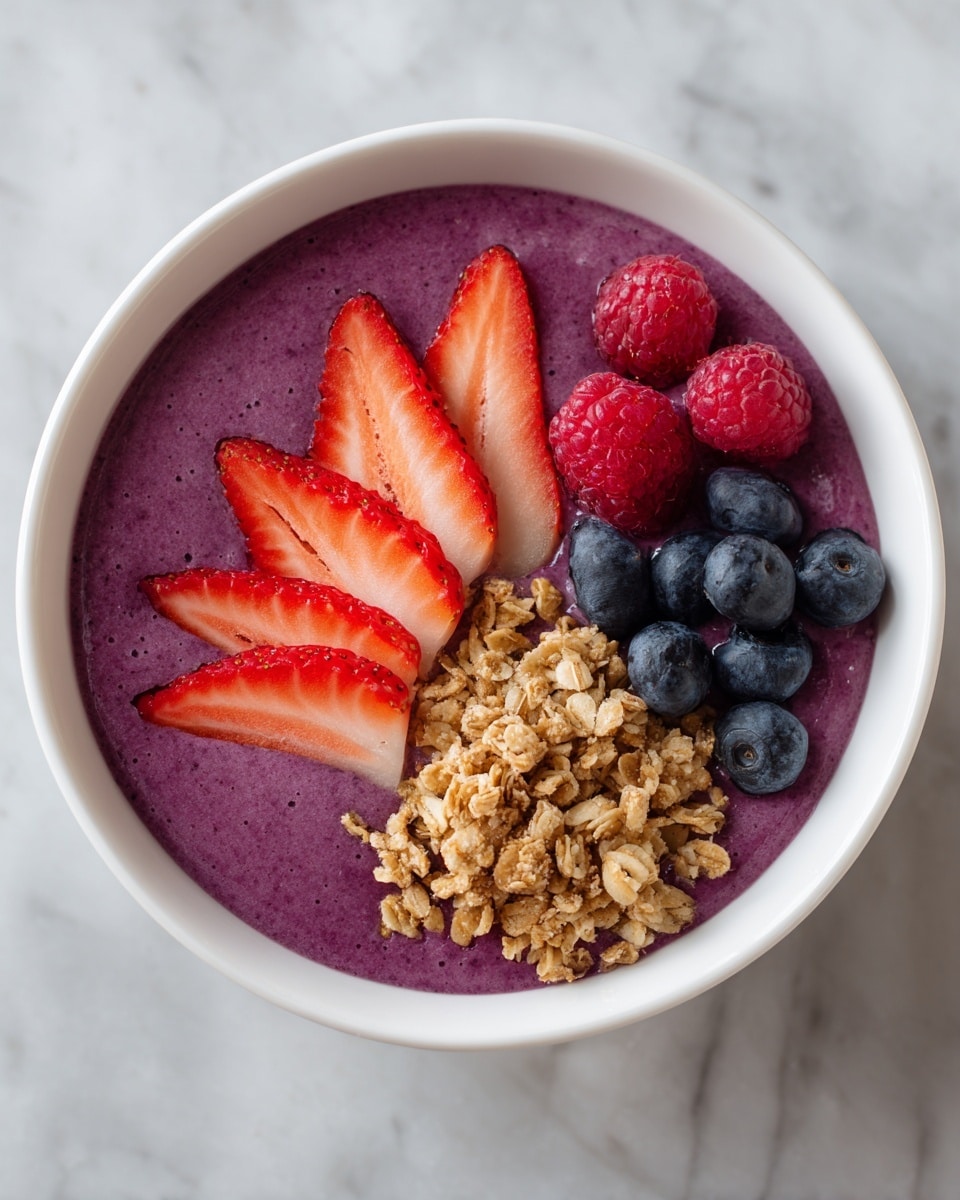 A white bowl filled with a thick, smooth purple smoothie base, topped with three main sections from left to right: a row of thinly sliced bright red strawberries, a small pile of light brown granola in the center with a rough texture, and a bunch of fresh, round blue blueberries. On top of the smoothie near the granola and blueberries are four round, bright red raspberries with a finely bumpy surface. The bowl sits on a white marbled surface. photo taken with an iphone --ar 4:5 --v 7
