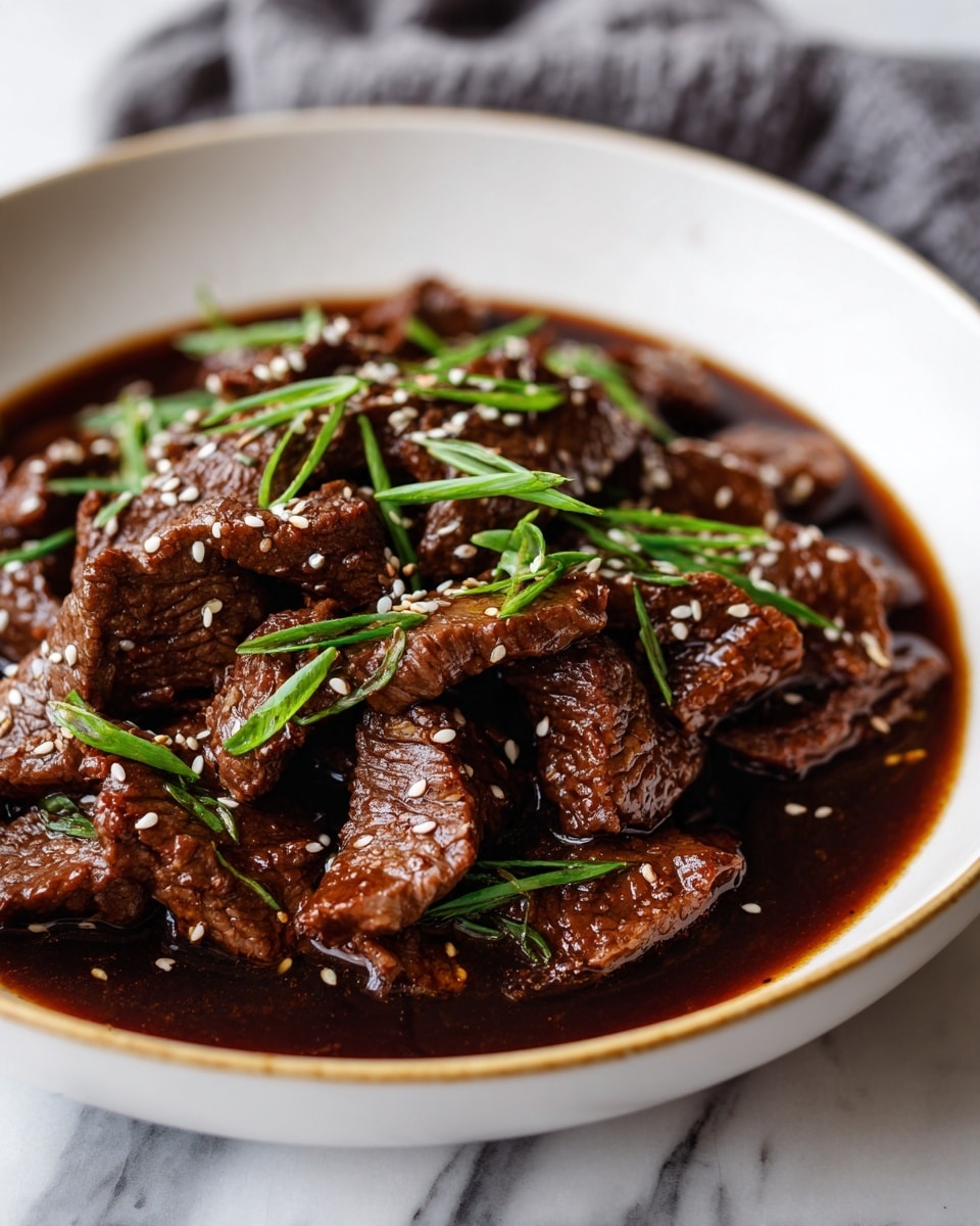 A bowl of dark brown beef strips cooked in glossy sauce fills the white bowl with a thin gold rim. The beef pieces have a tender, slightly oily texture with visible juices. Bright green chives are scattered on top of the beef, along with small white sesame seeds adding a touch of contrast. The bowl sits on a white marbled surface with parts of a light gray cloth visible nearby. photo taken with an iphone --ar 4:5 --v 7
