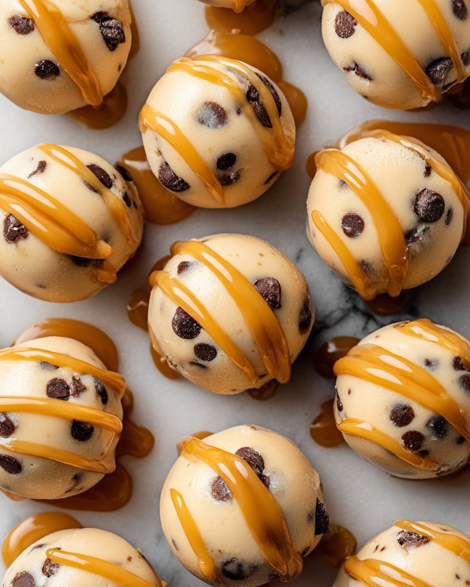 The image shows small frozen peanut butter yogurt bites in a close-up shot. Each bite is round and creamy light beige in color, with dark chocolate chips sprinkled inside. A caramel-colored drizzle is spread over the top, adding a shiny contrast. The bites are placed closely together on a white marbled surface. The texture looks smooth with small bumps from the chocolate chips. Photo taken with an iphone --ar 4:5 --v 7