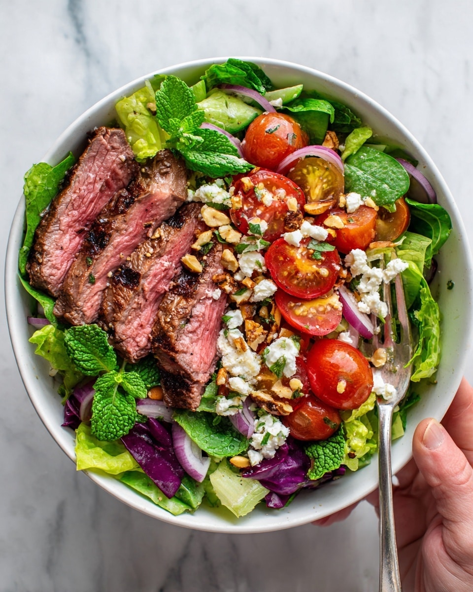 A white bowl holds a fresh salad with several layers. The bottom layer is mixed green leaves with red and light green lettuce. On top of the greens, there are slices of grilled steak arranged on one side, showing a pink inside and a browned outside with grill marks. Scattered around and over the steak and greens are halved cherry tomatoes, thin slices of red onion, and chopped nuts. Fresh mint leaves are spread across the salad, adding a touch of green. The bowl sits on a white marbled surface. Photo taken with an iphone --ar 4:5 --v 7