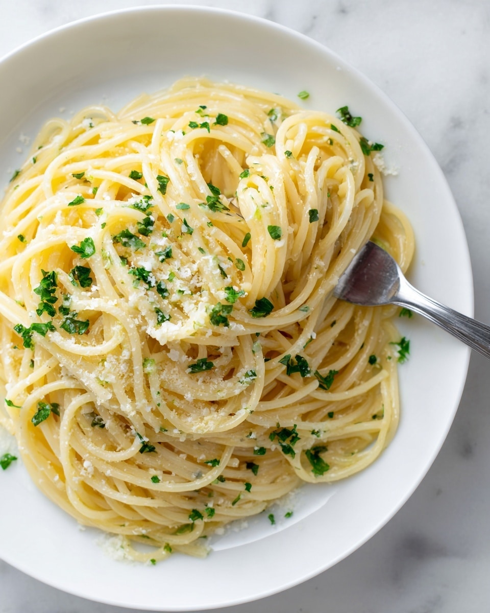 A white plate holds a serving of plain spaghetti piled high in loose, shiny strands of pale yellow pasta. The top layer is sprinkled with finely grated white cheese and small bits of fresh green parsley scattered evenly. A silver fork is partially visible on the right side, gently holding up a swirl of the spaghetti. The background features a white marbled texture surface. photo taken with an iphone --ar 4:5 --v 7