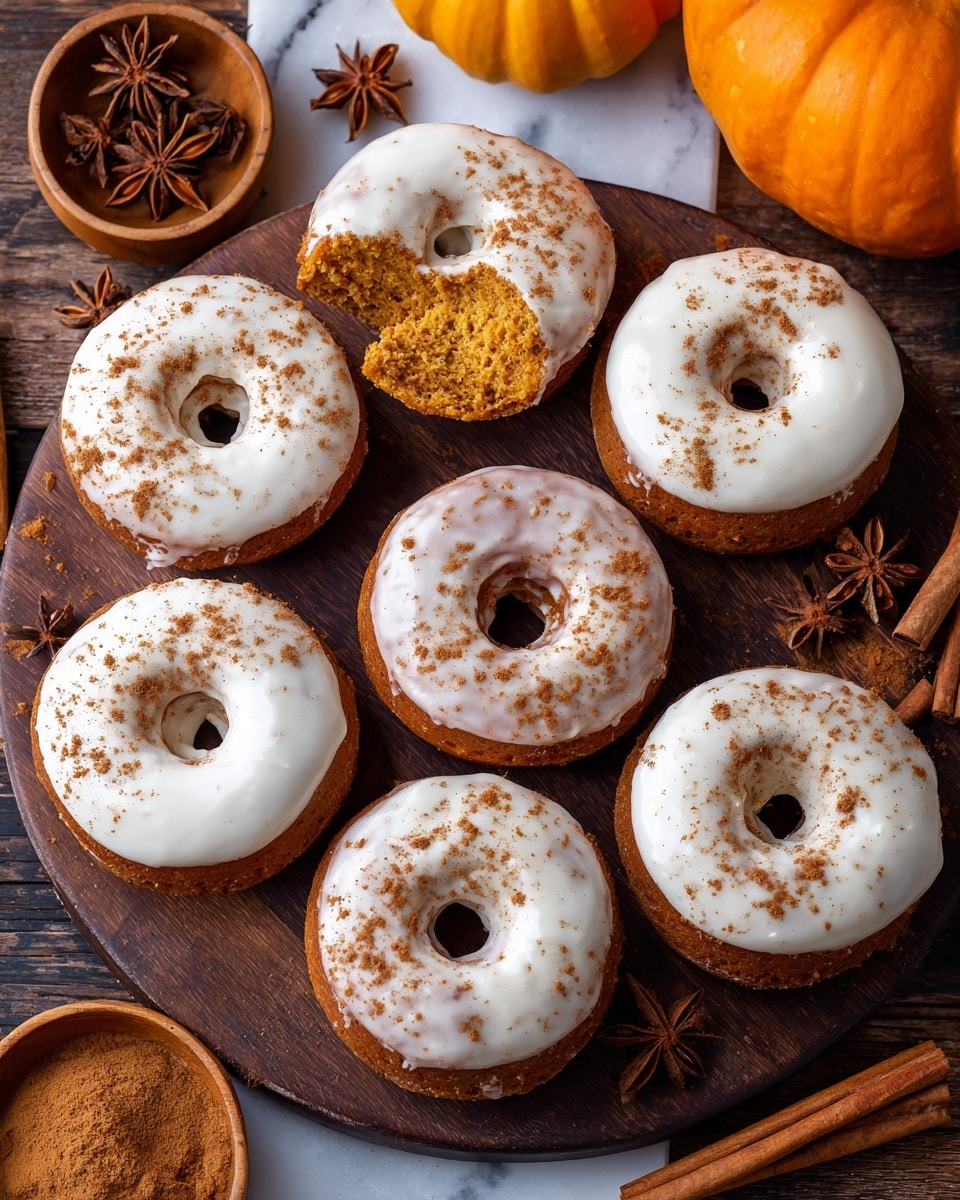The image shows six pumpkin donuts arranged on a dark wooden surface with a white marbled texture. Each donut has one thick layer of smooth, cream-colored icing covering the top, sprinkled lightly with cinnamon powder. The donut dough is a warm pumpkin orange-brown color. One donut has a bite taken out of it, showing its soft texture inside. Around the donuts, there are whole star anise and cinnamon sticks in a round wooden bowl, and a small wooden bowl filled with cinnamon powder. A bright orange pumpkin is partially visible in the top right corner. Photo taken with an iphone --ar 4:5 --v 7