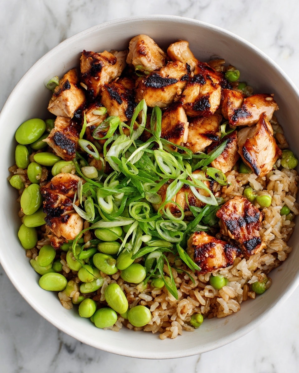 A close-up view of a white bowl filled with a dish featuring three main layers: the base layer is a bed of small brown grains, cooked to a soft texture with a slightly shiny appearance; the middle layer consists of round, light brown grilled chicken pieces with visible char marks, mixed evenly throughout; the top layer is scattered with bright green peas and edamame, along with thinly sliced green onion strips adding sharp freshness on top. The dish shows a mix of warm brown and fresh green colors with varied textures, all set against a white marbled background. photo taken with an iphone --ar 4:5 --v 7