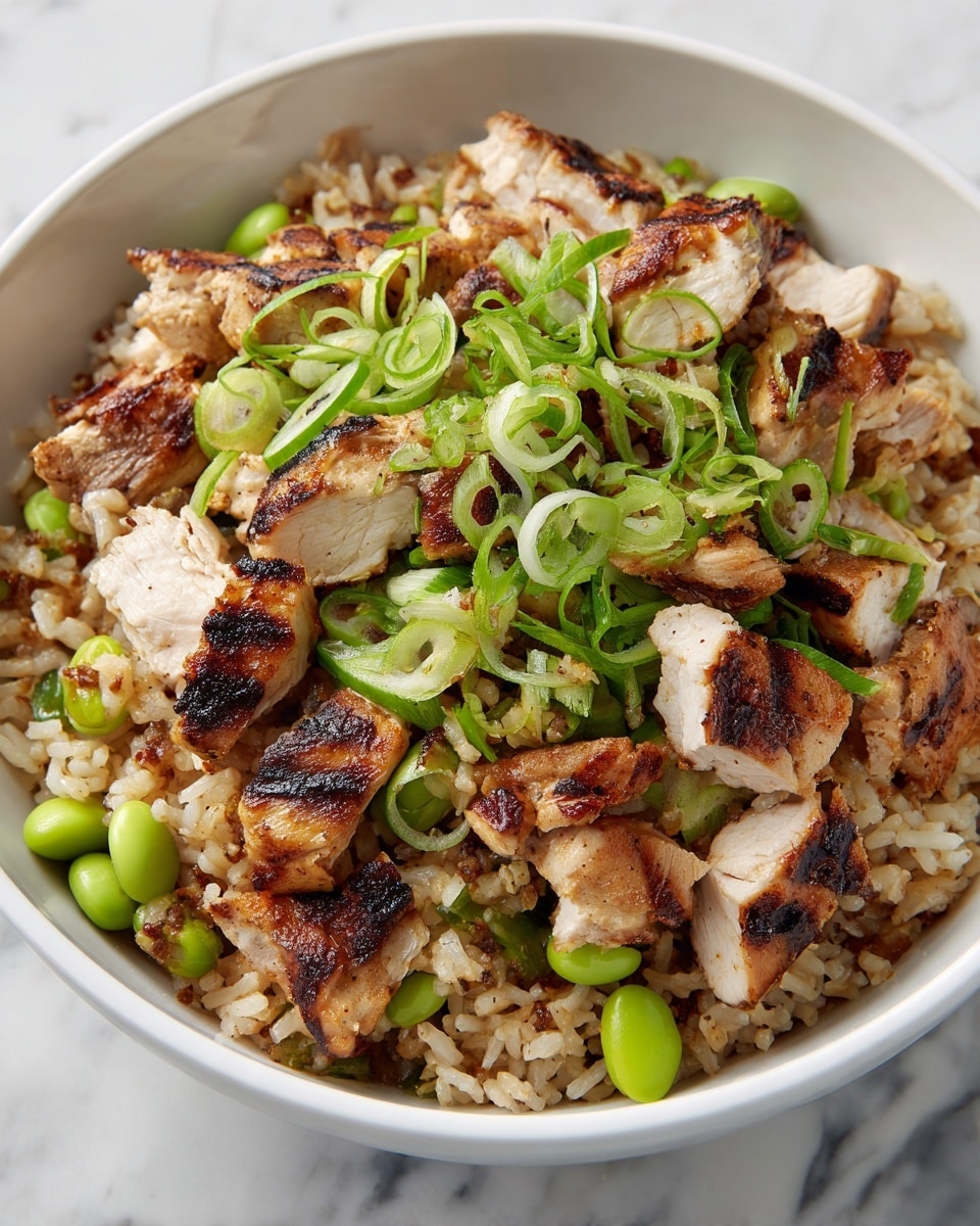 The dish is a close-up of a bowl filled with three main layers. The bottom layer is brown cooked rice with a slightly sticky and grainy texture. On top of the rice, there are medium-sized pieces of grilled, light brown chicken with char marks showing a slightly crispy outside. Scattered throughout are green peas and edamame, adding spots of bright green color. The dish is garnished with thinly sliced green onions spread evenly over the top. The bowl is white, and the background is a white marbled texture. photo taken with an iphone --ar 4:5 --v 7